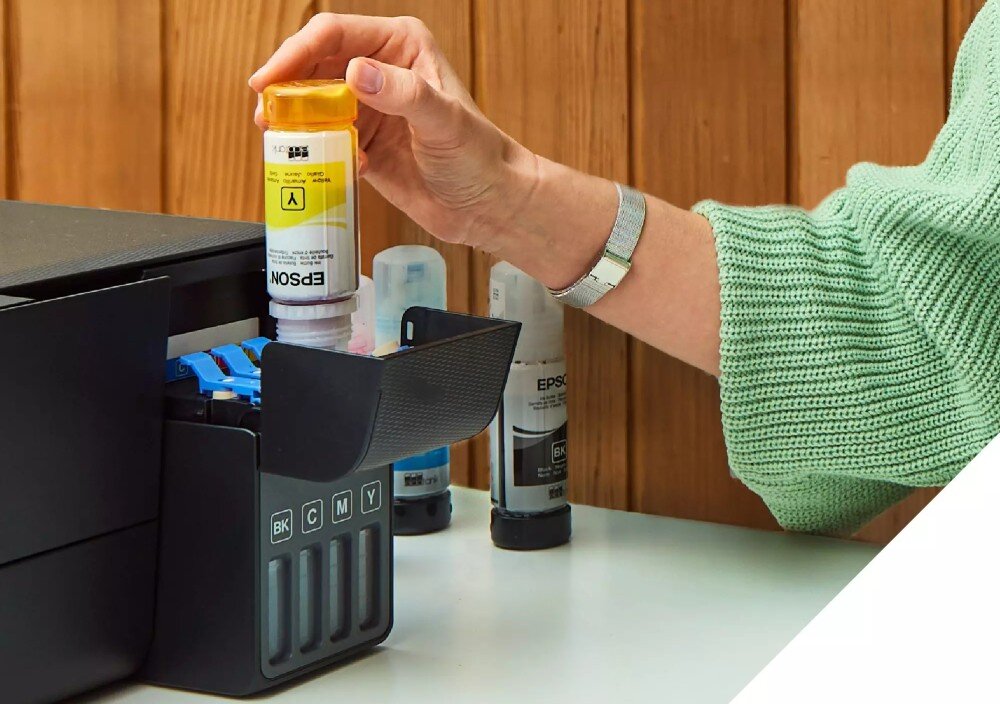 Osoba napełnia pojemnik na tusz w urządzeniu wielofunkcyjnym EPSON EcoTank. Widoczne są butelki z tuszem w różnych kolorach oraz oznaczenia BK, C, M, Y na urządzeniu.