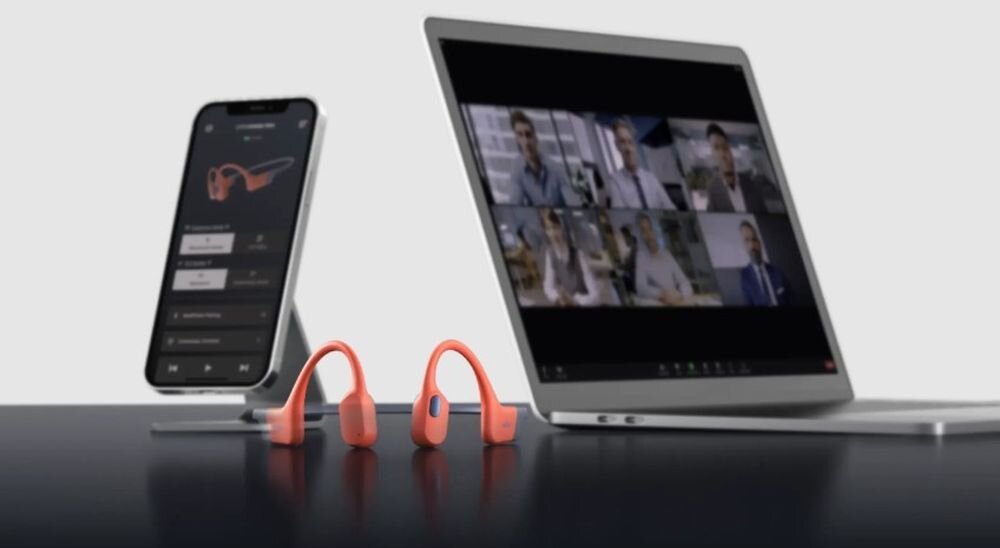 Słuchawki SHOKZ OpenSwim Pro multipoint dwa urządzenia Bluetooth zegarek GPS telefon, słuchawki leżące na blacie obok smartfona oraz laptopa