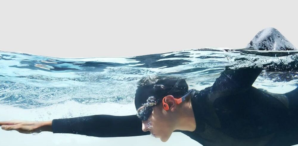Słuchawki SHOKZ OpenSwim Pro Bluetooth i MP3 32 GB do 8000 utworów tryb pod wodą, osoba z założonymi słuchAwkami kostnymi pływająca w basenie