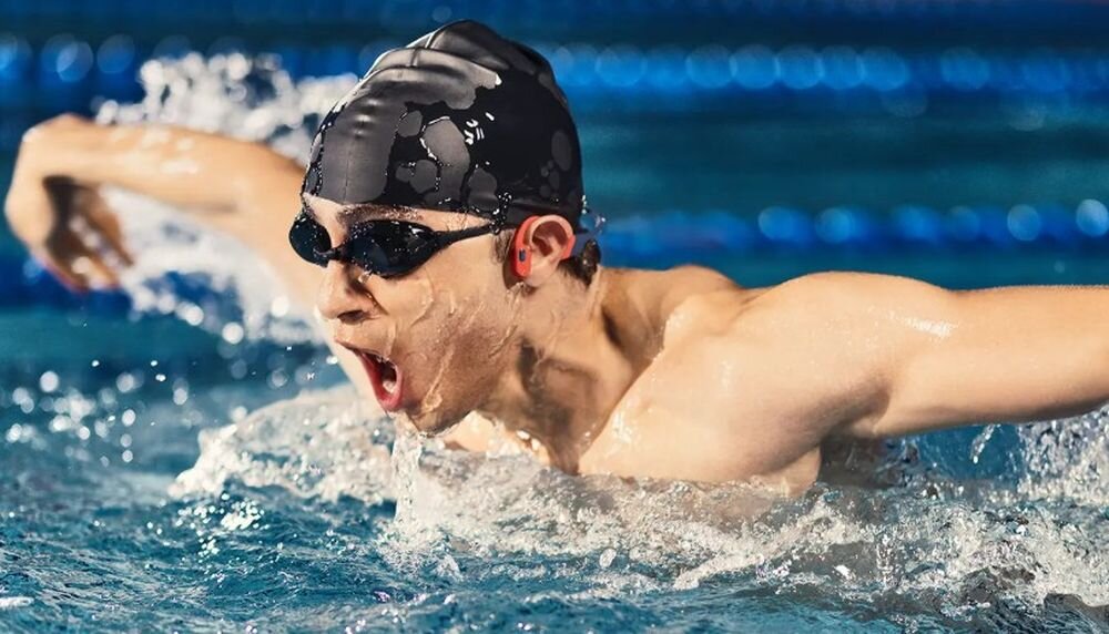 Słuchawki SHOKZ OpenSwim Pro pałąk nikiel tytan stabilne dopasowanie multisport, osoba z założonymi słuchAwkami kostnymi pływająca w basenie