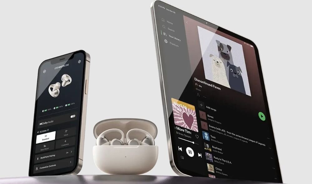 SHOKZ OpenDots One parowanie wielopunktowe dwa urządzenia płynne przełączanie, etui z funkją ładowania wraz ze słuchawkami stojące obok smartfona oraz tableta