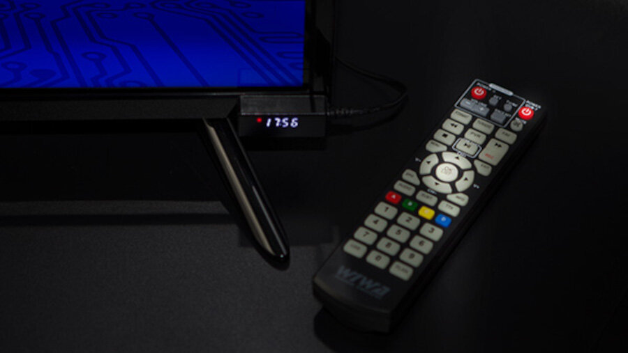 Na ciemnym tle widać telewizor z niebieskim ekranem i wyświetlaczem pokazującym \'17:56\'. Obok leży pilot z napisem \'WIWA\'.