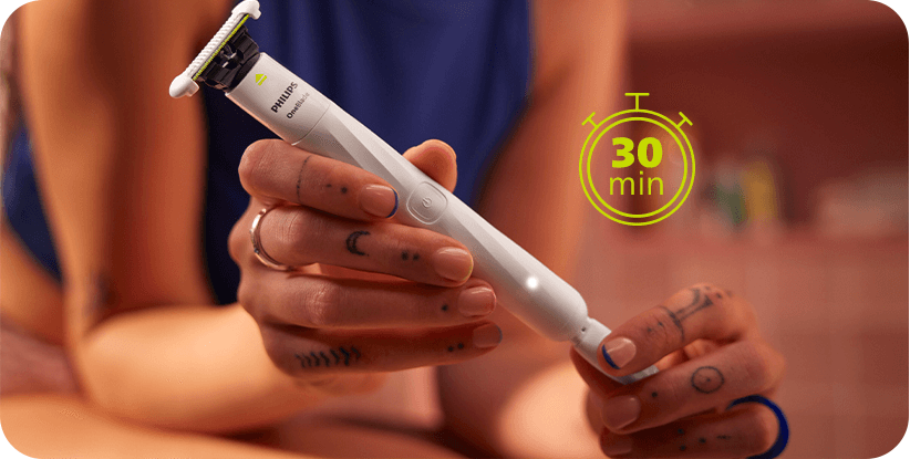 Osoba trzyma biały trymer z widocznym logo PHILIPS i napisem OneBlade. Obok znajduje się zielona ikona zegara z napisem \'30 min\'.