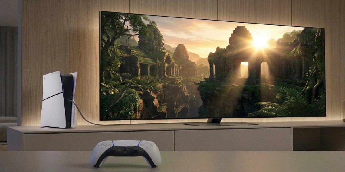 Biała konsola PS5 Digital Slim Edition i biały kontroler Dualsense leżące na stole, w tle widoczny jest telewizor wyświetlający grę.