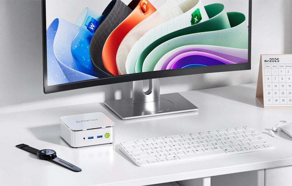 Komputer GMKTEC G10 Mały srebrny komputer ustawiony przy monitorze wyświetlającym kolorowe ikony aplikacji, obok klawiatura, zegarek i kalendarz, podzespoły, pamięć, dysk, procesor