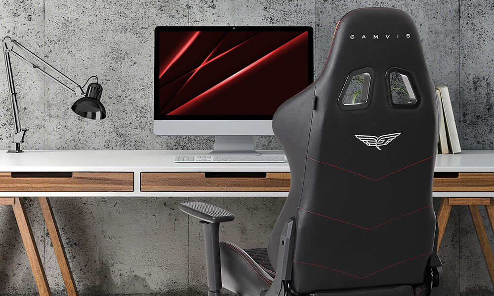 Fotel GAMVIS Phantom Large Czarny (czerwone elementy) prezentacja fotela w pokoju przy biurku szara ściana imitująca beton monitor lampka akcesoria wyścigowy charakter elegancja fotel klasy premium niezliczone godziny przed ekranem