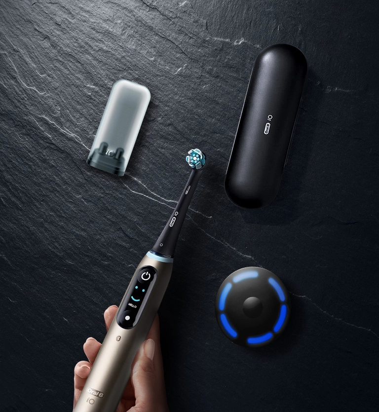 Zestaw Oral-B iO 10: szczoteczka, podróżne etui ładujące i czarna, okrągła ładowarka iSense na ciemnym, kamiennym tle.