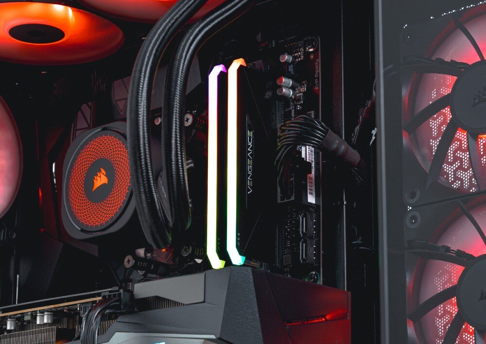 Komputer OPTIMUS E-Sport GB650T-CR4 zbliżenie na dwa moduły pamięci ram z napisem 'Vengeance' podświetlone kolorami tęczy, umieszczone obok blokopompy chłodzenia wodnego z logo pirackiego statku, płyta główna, pamięć RAM