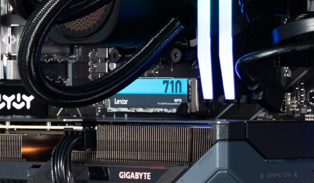 Komputer OPTIMUS E-Sport GB650T-CR4 Detal wnętrza komputera pokazujący dysk Lexar NM710 zamontowany w gnieździe płyty głównej nad kartą graficzną, oświetlony przez sąsiednie elementy ARGB, dysk, pojemność, prędkość