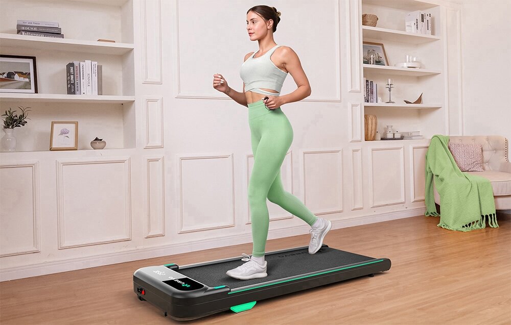 Bieżnia elektryczna UREVO Spacewalk E4 550W 6 km-h pokój osoba korzysta z bieżni w tle regał fotel domowy trening niewielka bieżnia