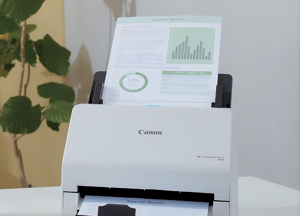 Skaner CANON R30 Zbliżenie na górną część białego skanera z umieszczonym w podajniku kolorowym arkuszem zatytułowanym 'Annual Report', który zawiera wykresy słupkowe i kołowe, podajnik ADF, wydajność, rozmiar, rozdzielczość