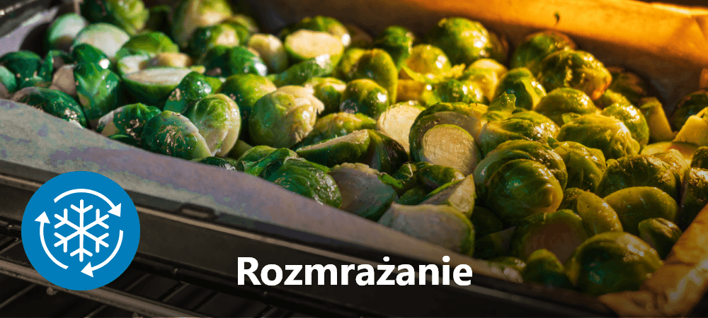 PIEKARNIK BEKO BBIM7300BD Blacha z pieczonymi warzywami (m.in. brukselką) w piekarniku, oświetlona ciepłym światłem. Na dole widoczny napis „Rozmrażanie” oraz ikona śnieżynki ze strzałkami, wskazujące funkcję rozmrażania w urządzeniu rozmrażanie żywności zachowanie struktury delikatny proces wygoda