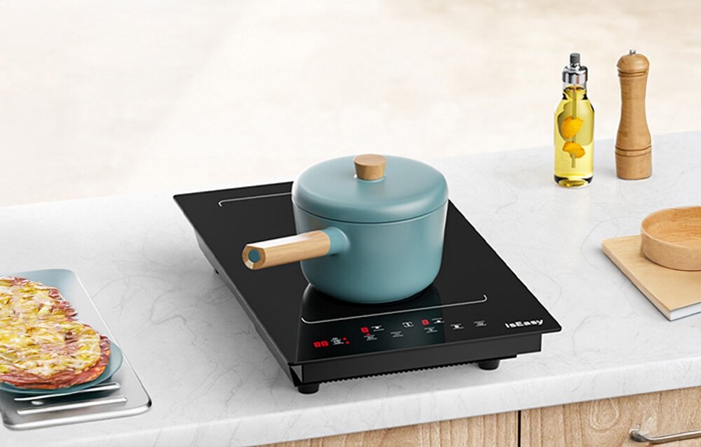 Płyta indukcyjna ISEASY LI2V-15 Na płycie indukcyjnej stoi jasny garnek z drewnianą rączką, a obok znajdują się oliwa, pieprz i inne kuchenne dodatki. Sprzęt ustawiono na blacie w jasnej, domowej kuchni blokada rodzicielska wskaźnik ciepła chłodzenie