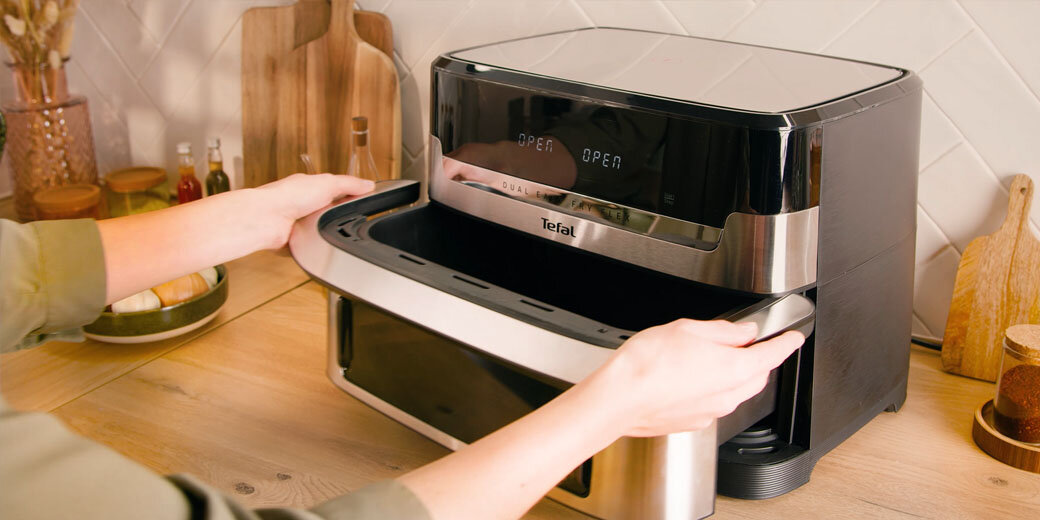 Osoba wyjmuje szufladę z frytkownicy Dual Easy Fry Flex EY922D. Urządzenie stoi na blacie, wyświetlacz pokazuje 