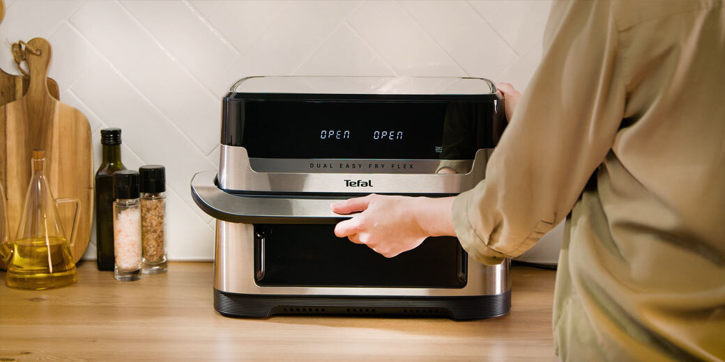 Frytkownica Dual Easy Fry Flex EY922D na kuchennym blacie, osoba trzyma dłoń na uchwycie urządzenia.