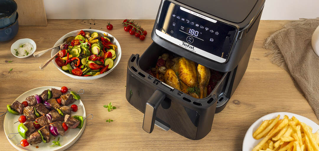 Na kuchennym blacie frytkownica Easy Fry Silence EY8468 z pieczonym kurczakiem, obok talerze z jedzeniem.