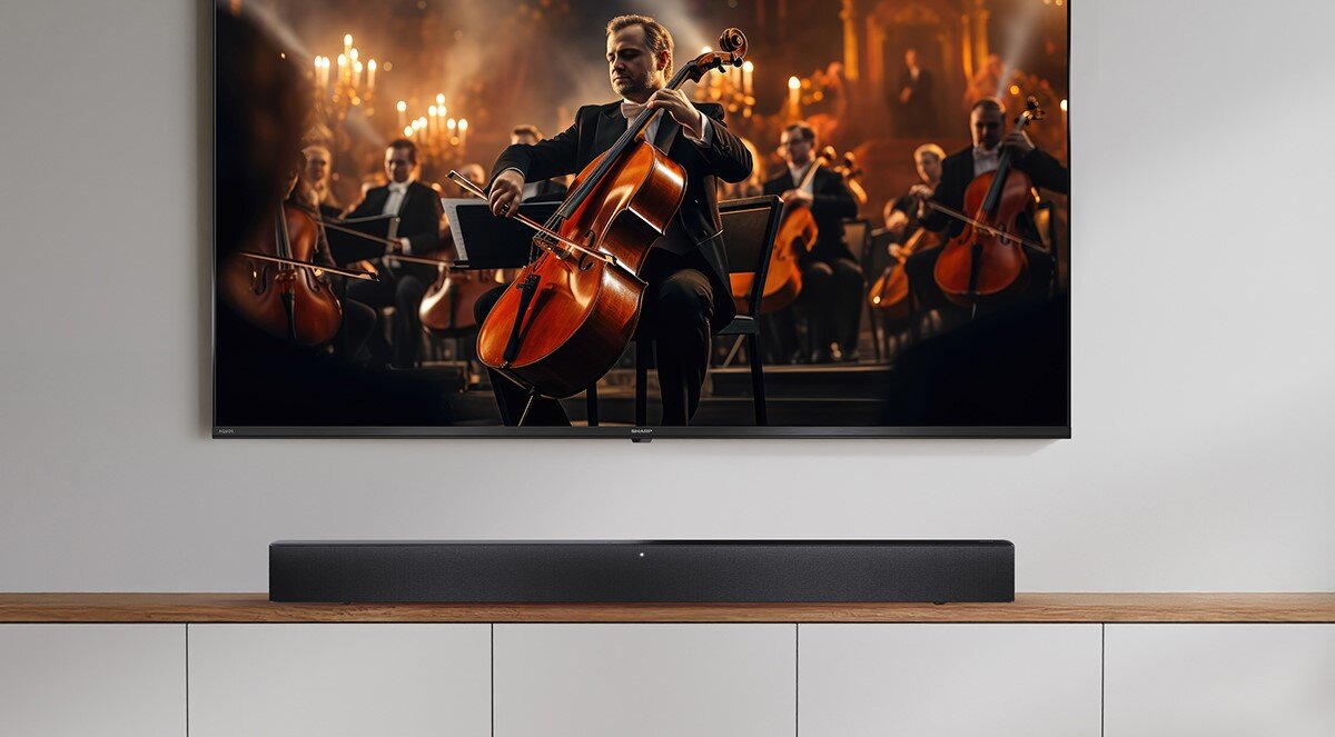 Soundbar SHARP HT-SBW312 moc 330W, dynamiczne brzmienie, filmy, muzyka, gry, soundbar stojący na szafce pod zawieszonym telewizorem