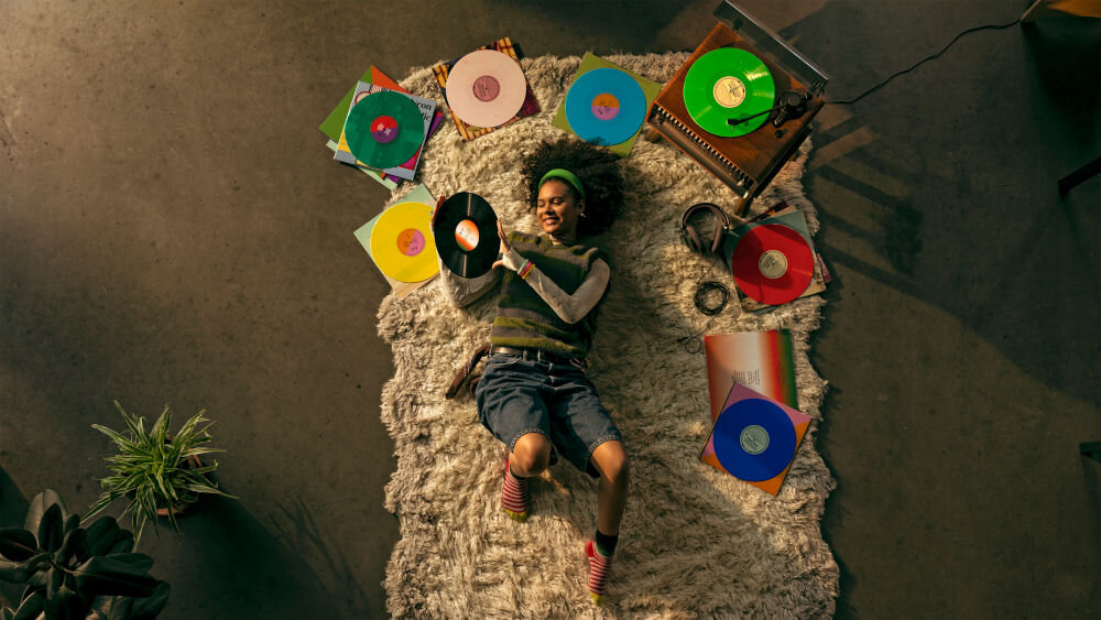 Gramofon PHILIPS TAV9000D/10 tworzywa z recyklingu opakowanie FSC ekologiczne materiały, osoba leżąca na dywanie z płytami gramofonowymi oraz gramofonem