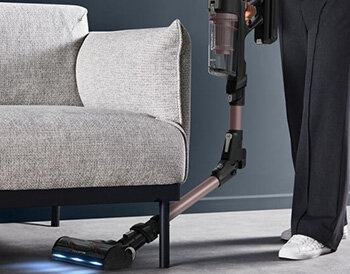 Osoba odkurza pod kanapą odkurzacz X-Force Flex 16.60 AeroSpin Aqua TY9CD9 ze zgiętą rurą.