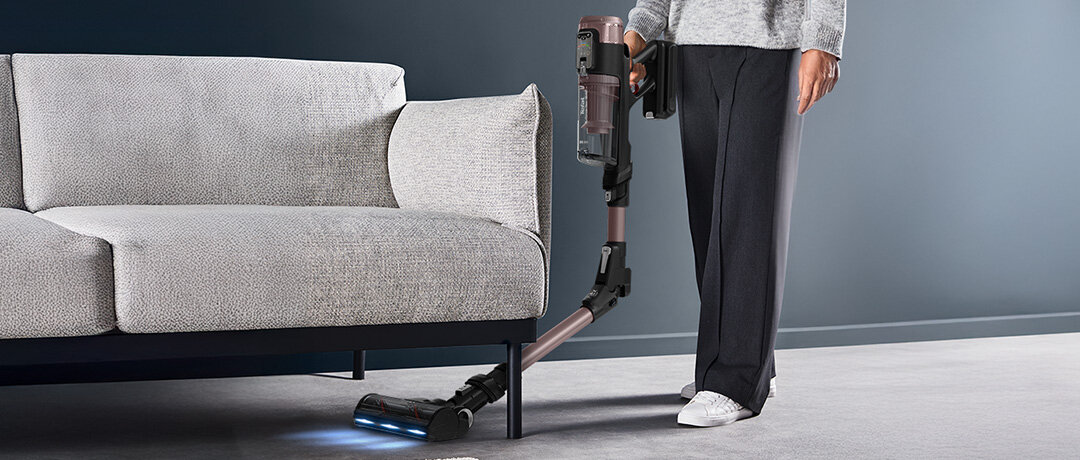 Mężczyzna odkurza przestrzeń pod kanapą odkurzaczem X-Force Flex 16.60 AeroSpin Aqua TY9CD9 ze zgiętą rurą.