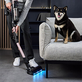 Osoba odkurza podłogę odkurzaczem X-Force Flex 16.60 AeroSpin Aqua TY9CD9 z podświetleniem. Na kanapie pies.