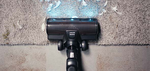 Odkurzacz z niebieskim światłem LED czyszczący dywan z piór. Na dywanie widoczne są białe pióra, a odkurzacz jest w trakcie ich usuwania.