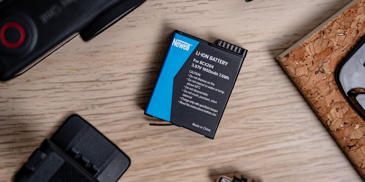Akumulator NEWELL zamiennik BCX204 do DJI Osmo Action 3/4/5 Pro, Akumulator Newell BCX204 do kamery Action 5 Pro leżący na jasnym, drewnianym blacie obok akcesoriów montażowych, moc, dynamika, nagrania, zasilanie