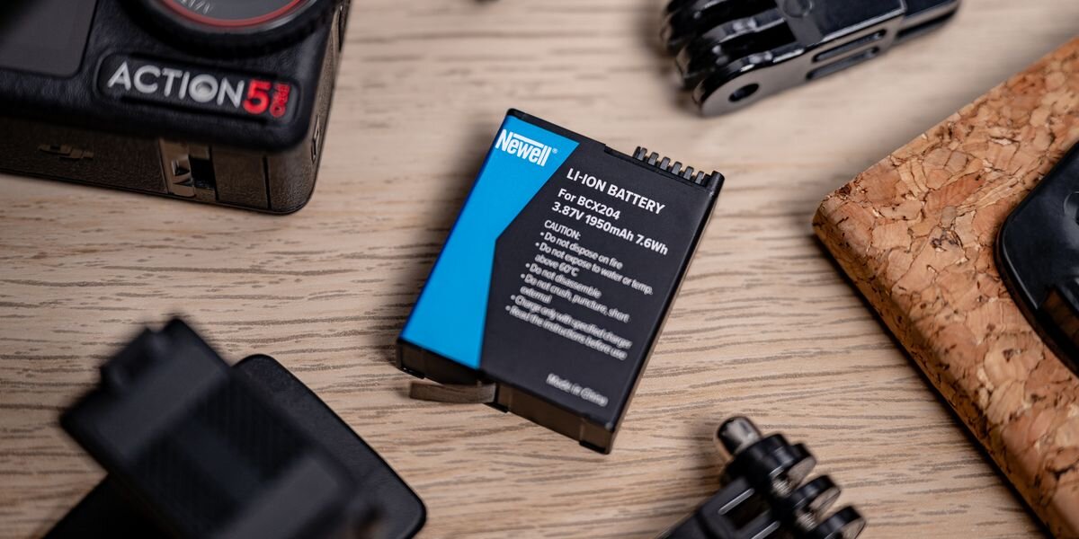 Akumulator NEWELL zamiennik BCX204 do DJI Osmo Action 3/4/5 Pro, Akumulator Newell BCX204 leżący na jasnym drewnianym blacie obok kamery Action 5 Pro i elementów montażowych, 1950mAh, Li-ion, 3,87V, sport