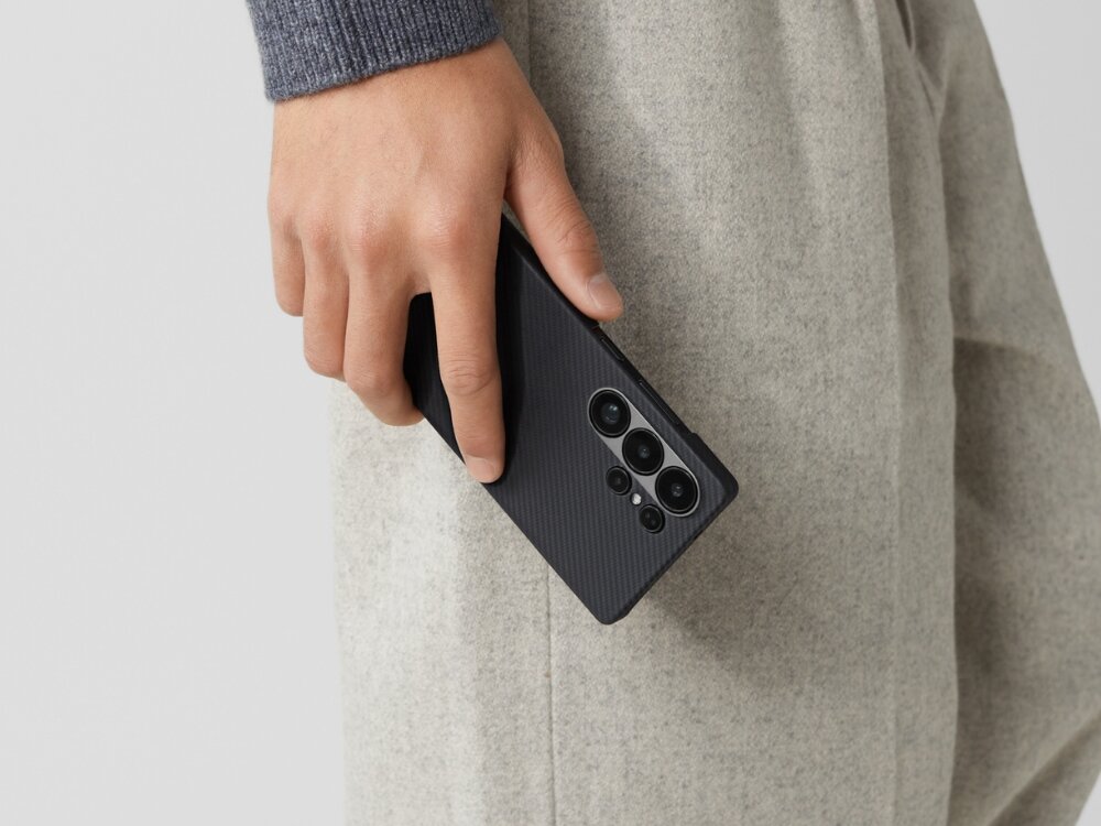 Etui PITAKA Ultra-Slim MagSafe
                telefon z etui trzymany w dłoni przy uchu na jasnym tle