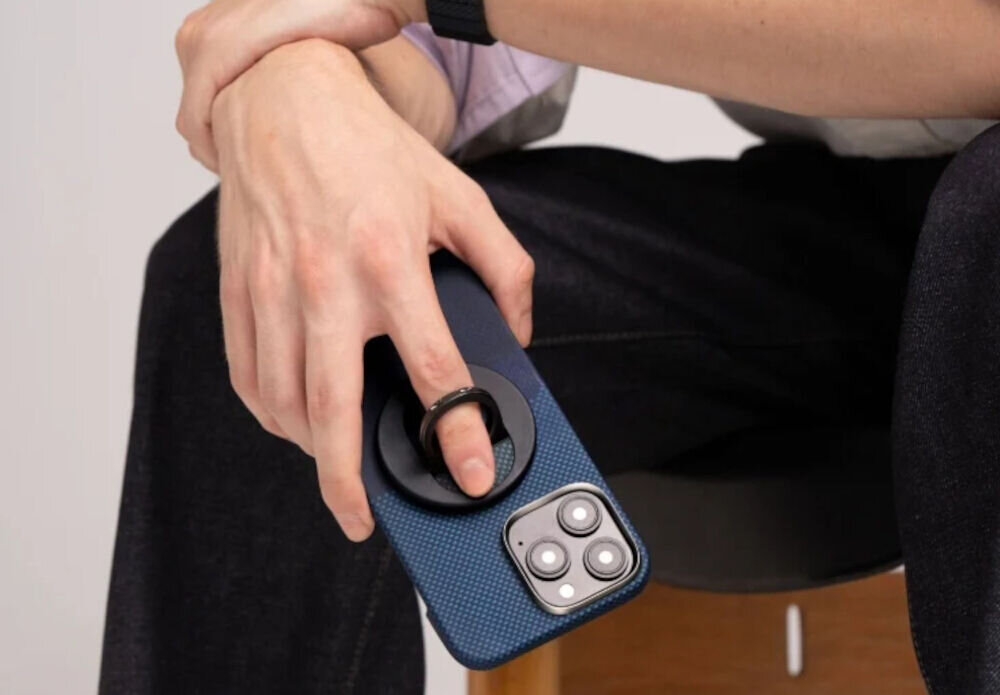 Uchwyt i podstawka PITAKA MagEZ Grip 3 MagSafe Czarno-niebieski telefon trzymany w dłoni przez mężczyznę palec przełożony przez uchwyt cienki uchwyt MagSafe z aramidu