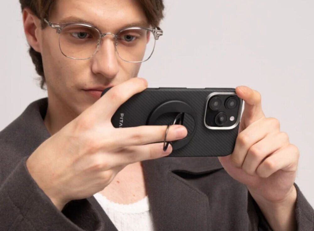 Uchwyt i podstawka PITAKA MagEZ Grip 3 MagSafe Czarno-szary mężczyzna trzymający telefon z przyczepionym uchwytem w dłoniach jasne tło Aramidowa konstrukcja i cienki profil uchwytu MagSafe waga grubość konstrukcja 2-pierścieniowa odpowiedni chwyt