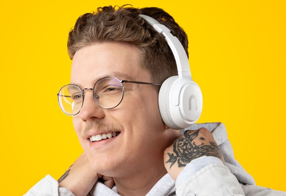 Słuchawki nauszne NICEBOY Hive Prodigy 4 kodek AAC SBC jakość dźwięku Apple, osoba z założonymi słuchawkami nausznymi na żółtym tle