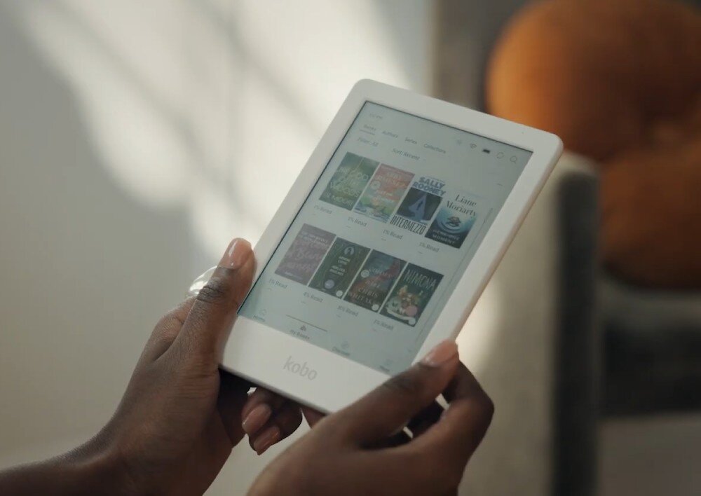 Czytnik e-booków KOBO Clara Colour Osoba trzyma w dłoniach biały czytnik e-booków z widocznymi okładkami książek na ekranie, wygląd, opis