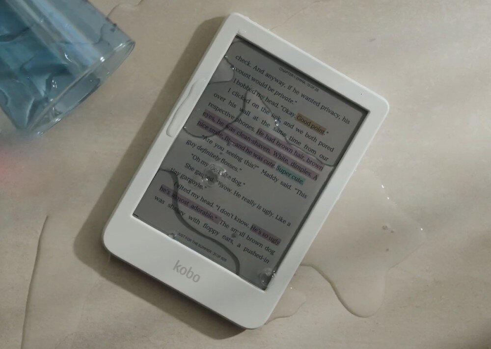 Czytnik e-booków KOBO Clara Colour Biały czytnik e-booków leży na mokrej powierzchni z kroplami wody na ekranie obok przewróconej szklanki, wodoodporność, szczelność