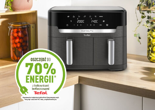 Na blacie kuchennym stoi czarna frytkownica beztłuszczowa z dwoma uchwytami i wyświetlaczem pokazującym temperatury 200°C i 140°C. Obok znajduje się zielony okrągły znak z napisem \'OSZCZĘDŹ DO 70% ENERGII z frytkownicami beztłuszczowymi Tefal\'.