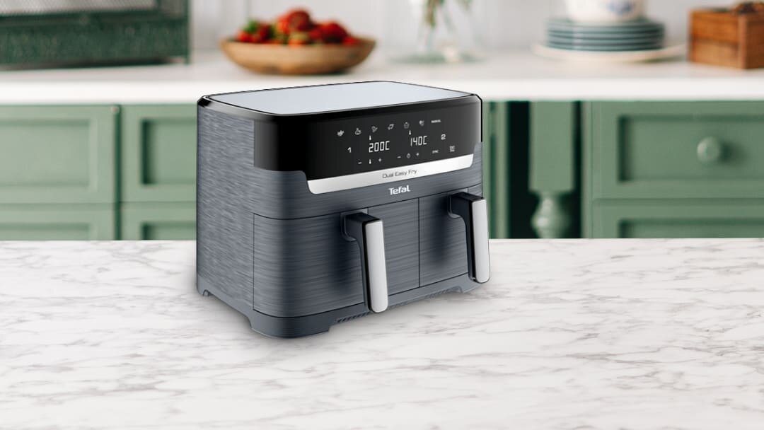 Na blacie kuchennym stoi frytkownica beztłuszczowa z dwoma uchwytami i panelem dotykowym. Na panelu widoczny jest tekst: \'200C\', \'140C\', \'Dual Easy Fry\', \'Tefal\'.