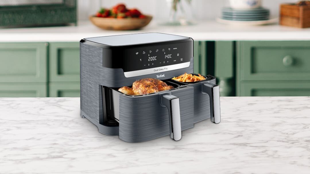 Na blacie kuchennym stoi frytkownica beztłuszczowa z dwoma wysuniętymi koszami, w których znajdują się pieczony kurczak i frytki. Na panelu sterowania widoczne są ustawienia temperatury 200°C i 180°C oraz logo Tefal.