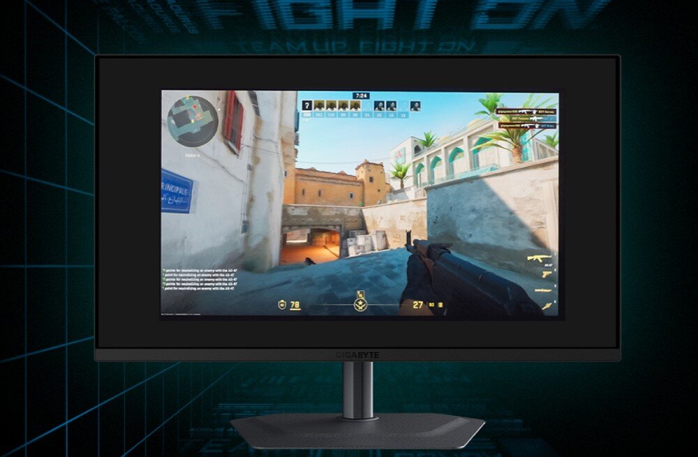 Monitor GIGABYTE MO27Q2A Na pierwszym planie monitor z oknem gry przedstawiającej korytarz uliczny i interfejs z mapą, w tle ciemna siatka linii tworząca perspektywę