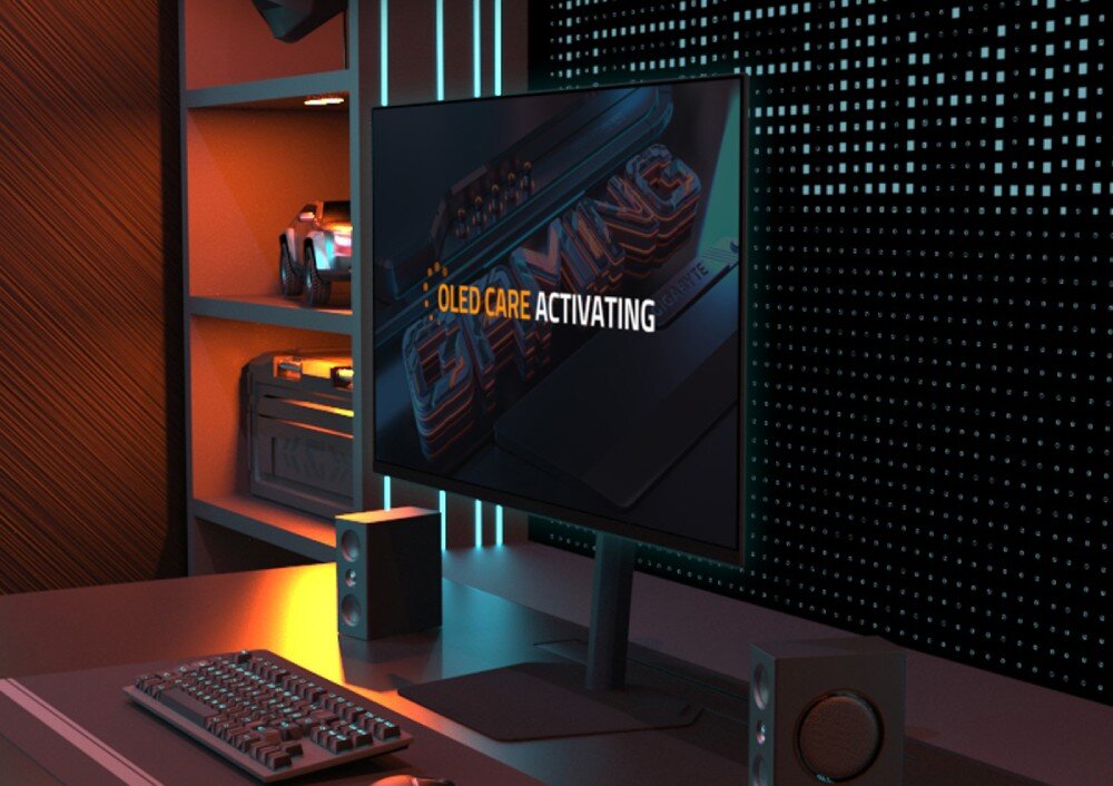 Monitor GIGABYTE MO27Q2A Na pierwszym planie monitor na biurku z napisem 'OLED CARE ACTIVATING' na ekranie, w tle półki z figurkami i ściana z perforowanym wzorem świetlnym