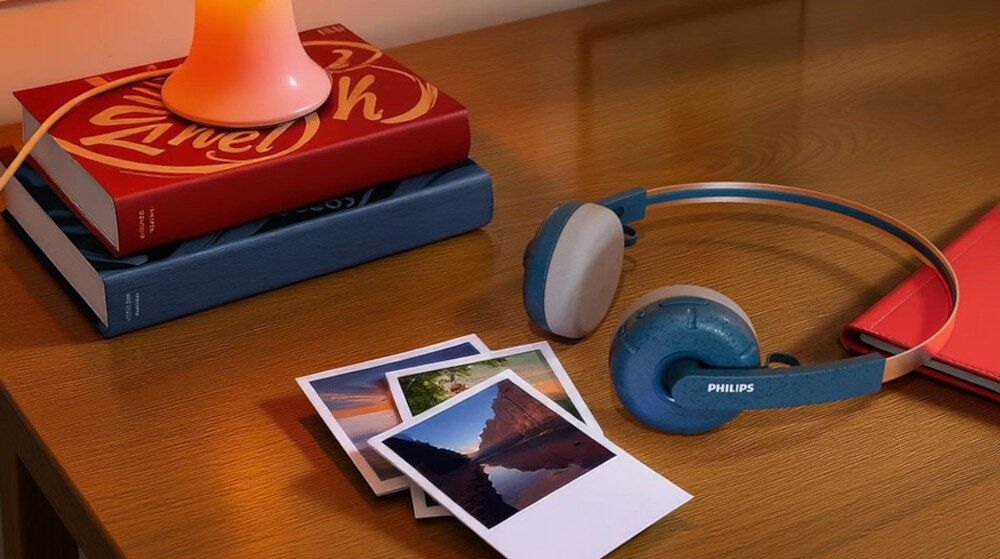 Słuchawki nauszne PHILIPS TAH2000TL/00 design retro i wysokiej jakości dźwięk z 40 mm przetwornikami, słuchawki leżące na stole obok fotografii