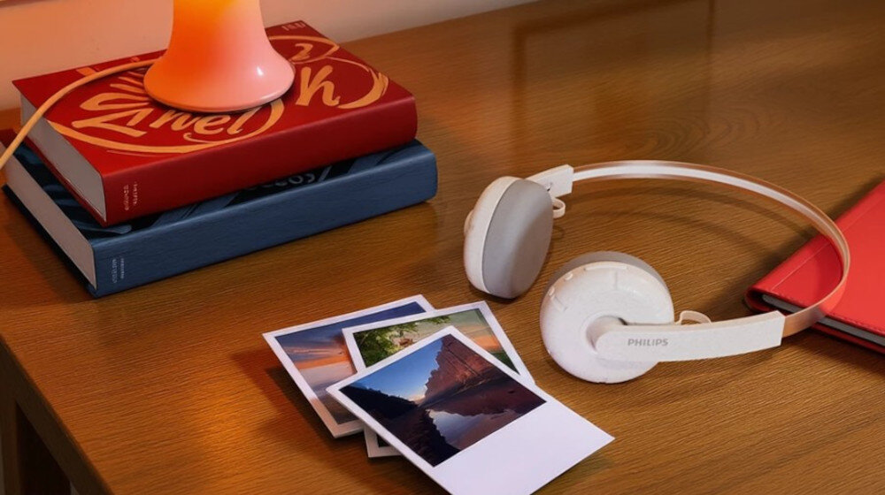Słuchawki nauszne PHILIPS TAH2000WT/00 design retro i wysokiej jakości dźwięk z 40 mm przetwornikami, słuchawki leżące na stole obok fotografii