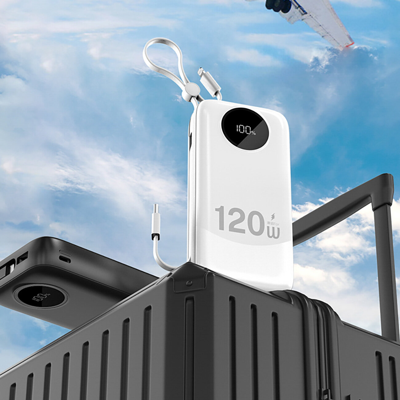 Biały powerbank z wyświetlaczem pokazującym \'100%\' i oznaczeniem \'120W\' stoi na walizce. W tle widać niebo z przelatującym samolotem.