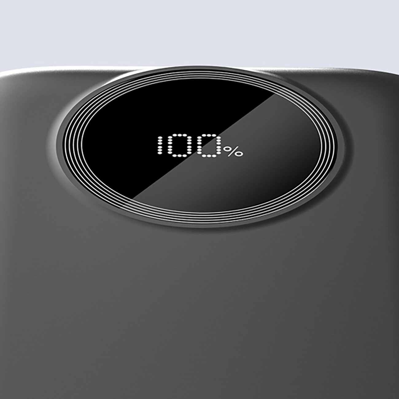 Obraz przedstawia czarny powerbank z owalnym wyświetlaczem pokazującym \'100%\'.