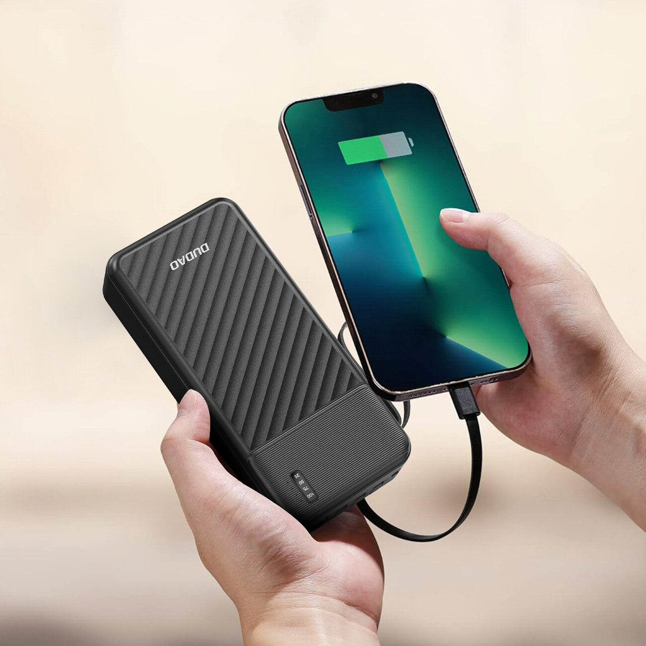 Osoba trzyma czarny powerbank z logo \'DUDAO\' oraz smartfon z ikoną ładowania baterii. Powerbank ma wbudowane kable i teksturowaną powierzchnię.