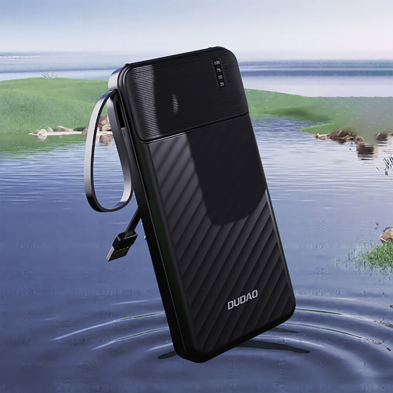 Czarny powerbank z wbudowanymi kablami unosi się nad wodą, na tle zielonego krajobrazu. Na urządzeniu widoczne jest logo \'DUDAO\' oraz wskaźnik poziomu naładowania z wartościami 100, 75, 50, 25.