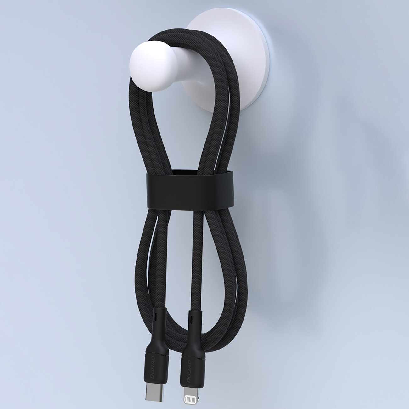 Czarny kabel USB-C do Lightning zawieszony na białym uchwycie ściennym. Kabel jest spięty czarną opaską, a na końcówkach widoczne są napisy \'Dudao\'.