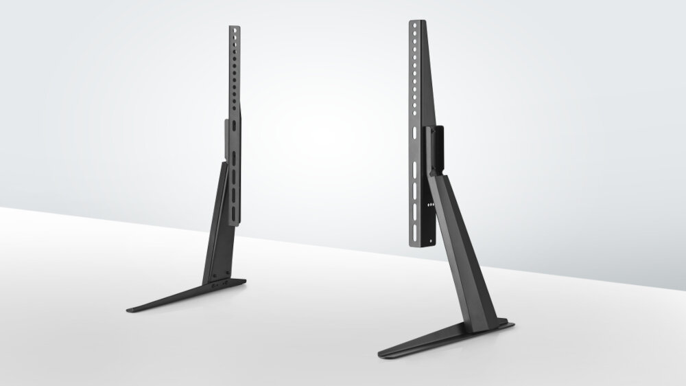 Na obrazie widoczne są dwa czarne stojaki podłogowe do telewizorów, ustawione na białej powierzchni. Stojaki mają prostą konstrukcję z pionowymi i poziomymi elementami, przeznaczone do montażu telewizorów.