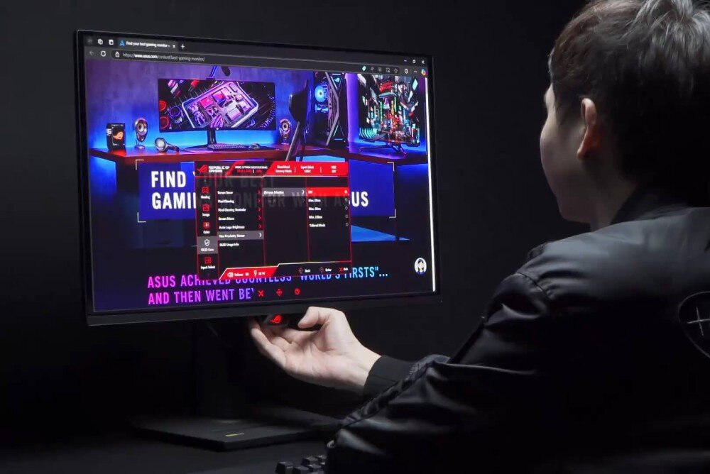 Osoba obsługuje monitor, na którym wyświetlana jest strona internetowa z grafiką komputerową i tekstem \'FIND GAMING MONITORS\'. Na ekranie widoczny jest również czerwony panel ustawień monitora.