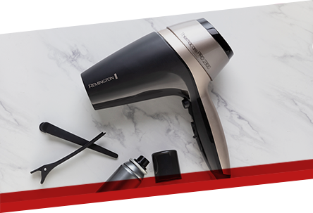 Na marmurowej powierzchni leży suszarka do włosów z napisem \'REMINGTON\' oraz \'THERMACARE PRO\'. Obok znajdują się akcesoria: koncentrator, dyfuzor i klips do włosów.