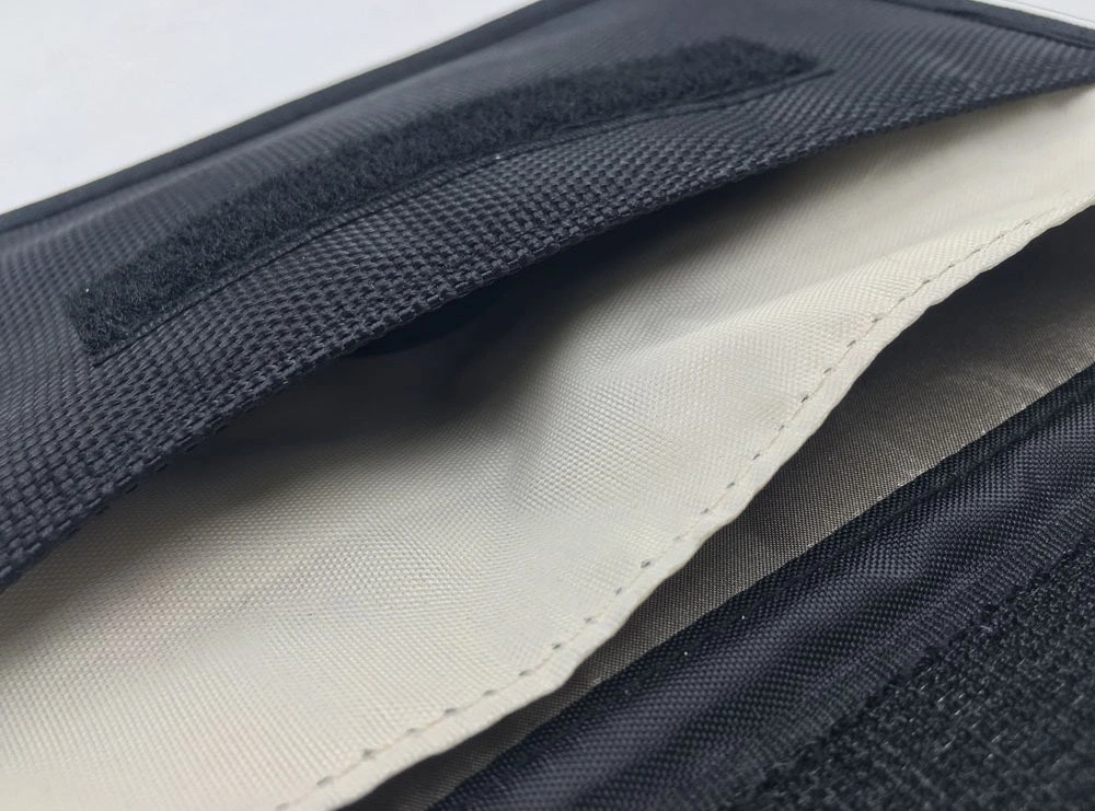 Czarne etui z materiału z jasnym wnętrzem, widoczny rzep na krawędzi.